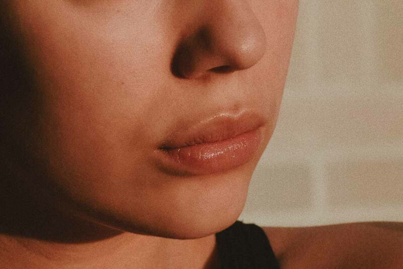 Close-up of a person's lips and nose, highlighted by warm, soft lighting that enhances the skin's natural texture.