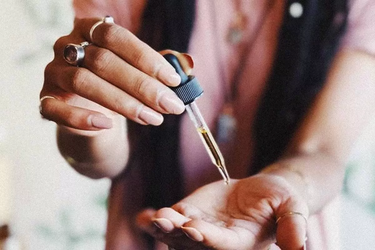 Close-up of a person's hands using a dropper to apply organic facial oil, emphasizing natural skin care routine.