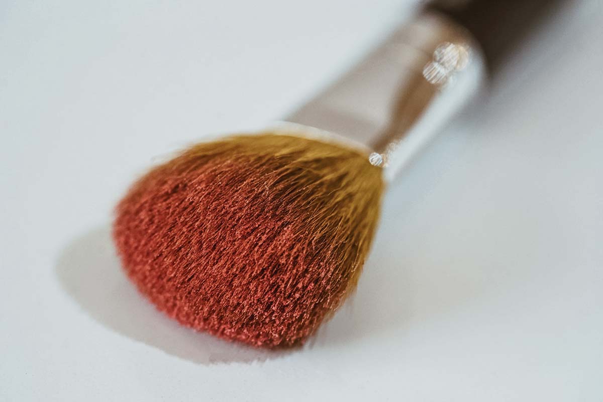 A makeup brush with bristles partially coated in red pigment use for applying makeup products.