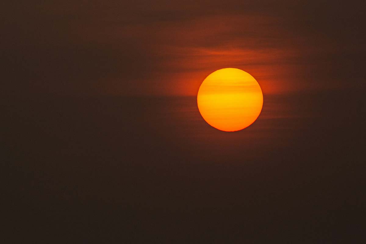 A large, radiant sun suspended in a hazy sky, emits a warm, orange glow, illuminating the surrounding atmosphere with soft, diffused light.