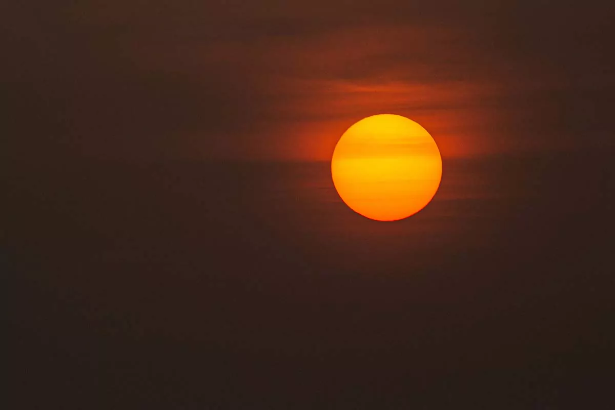 A large, radiant sun suspended in a hazy sky, emits a warm, orange glow, illuminating the surrounding atmosphere with soft, diffused light.