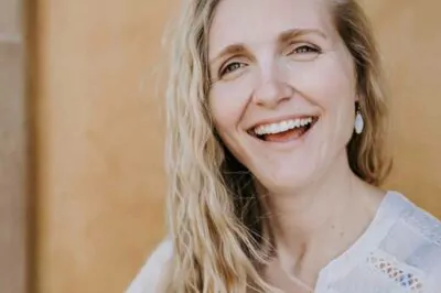 A woman with blonde hair and casual attire, smiling warmly, representing healthy, radiant skin