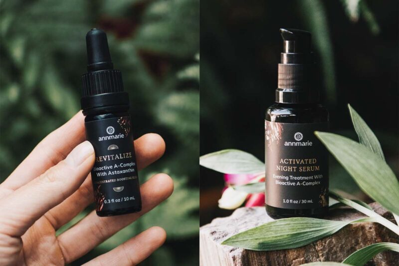 Hand holding Annmarie Revitalize Bioactive A-Complex with Astaxanthin, set against a leafy backdrop" and "Annmarie Activated Night Serum.
