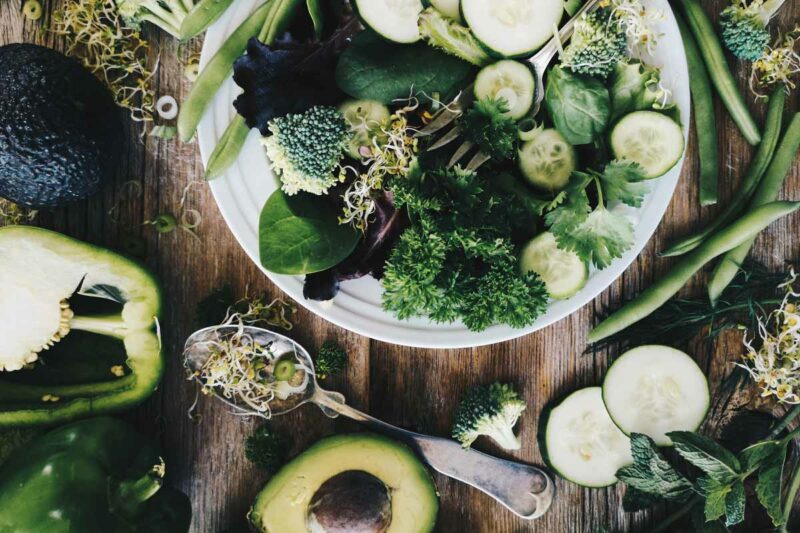 Assorted fresh green vegetables and sprouts arranged on a rustic wooden table, emphasizing a healthy diet.