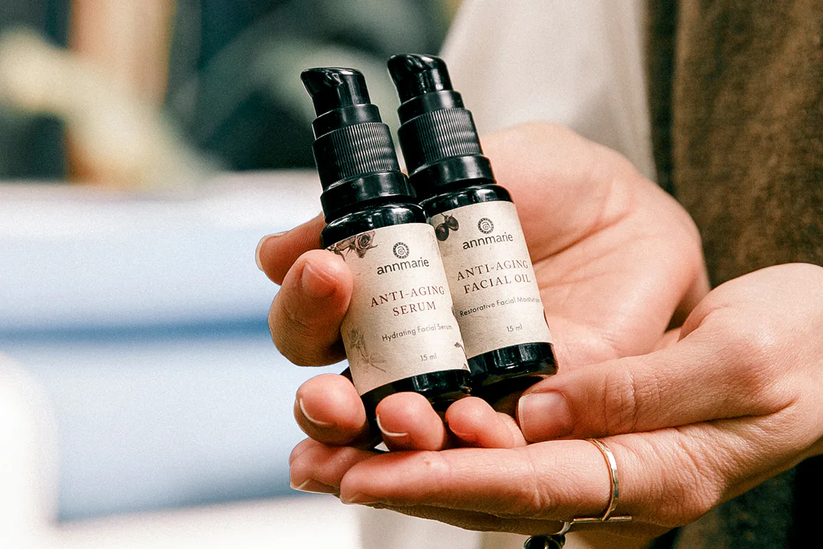 Two hands holding both the Anti-Aging Serum bottle and the Anti-Aging Facial Oil bottle